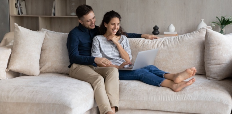 A couple sat on the sofa looking at a laptop together