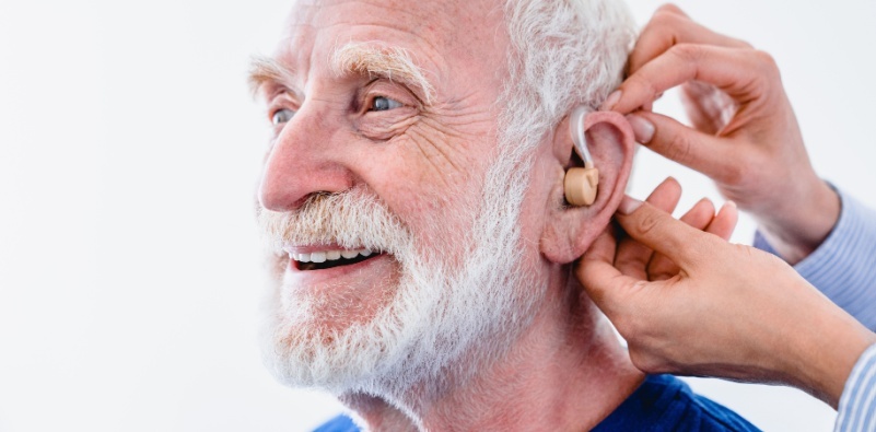 Audiologist providing hearing aid to a happy older gentleman