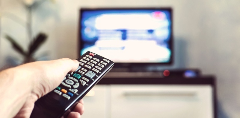 Person holding a TV remote to turn up the volume